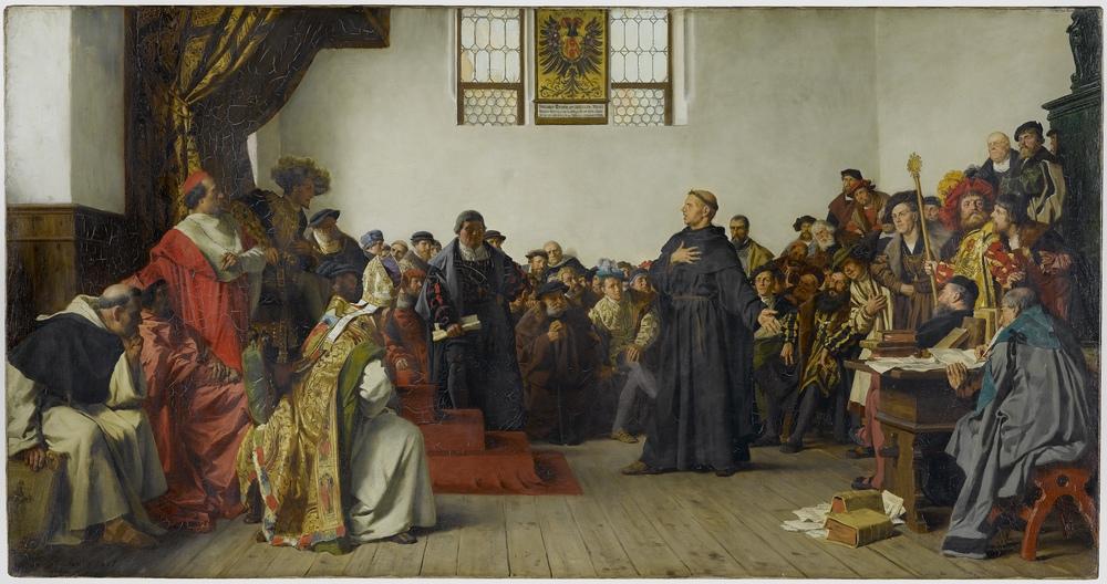 In einem Raum voller Menschen steht Luther auf der rechten Seite vor dem Herrscher.