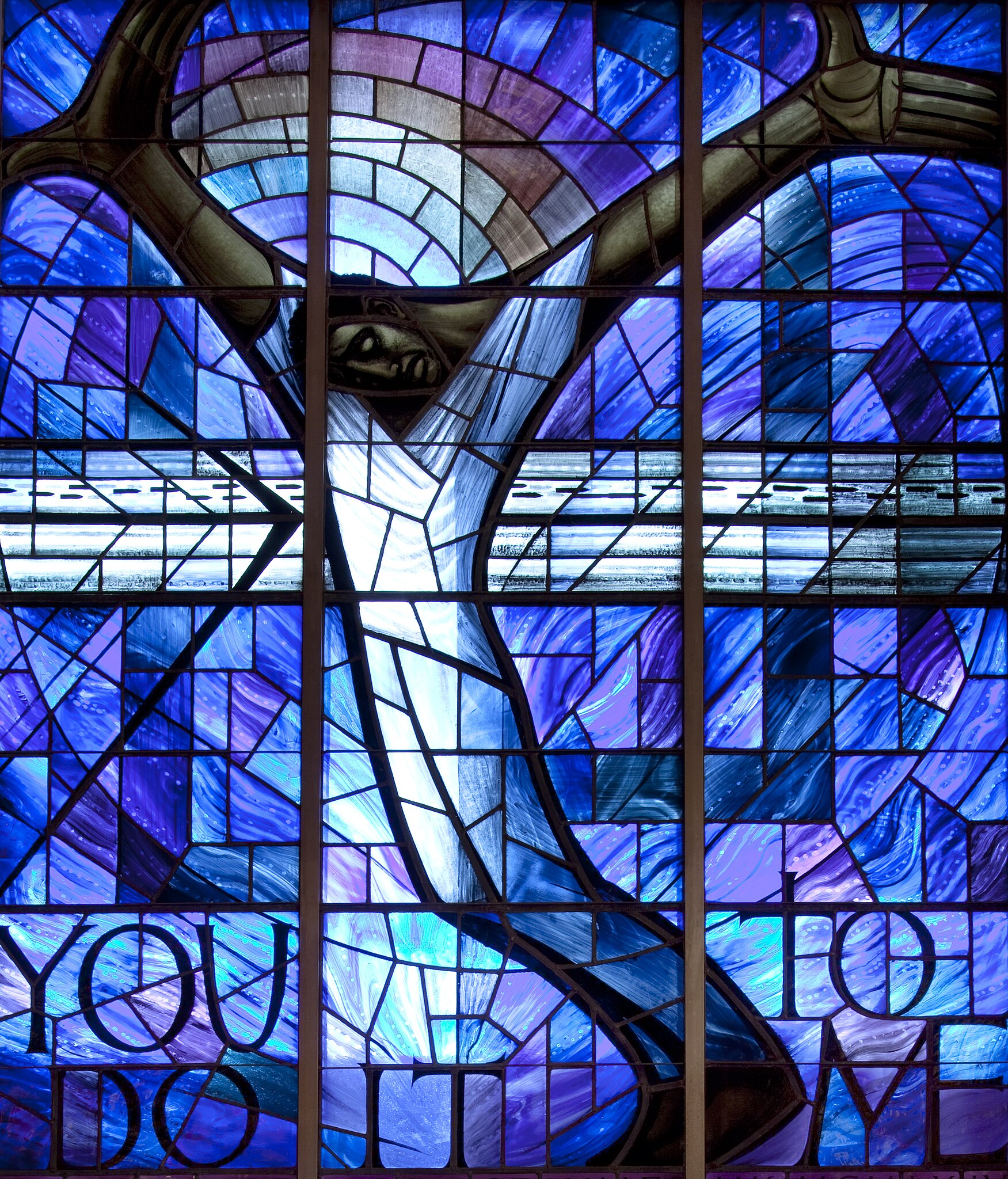 Das Kirchenfenster zeigt einen Schwarzen Christus, dessen Hände Widerstand und Versöhnung zu signalisieren scheinen – und deutet im Regenbogen auch auf Gottes Bundestreue sowie im Schriftzug „You do it to me/Das habt ihr mir getan“ auf Jesu eschatologische Rede vom Weltgericht (Mt 25,40).